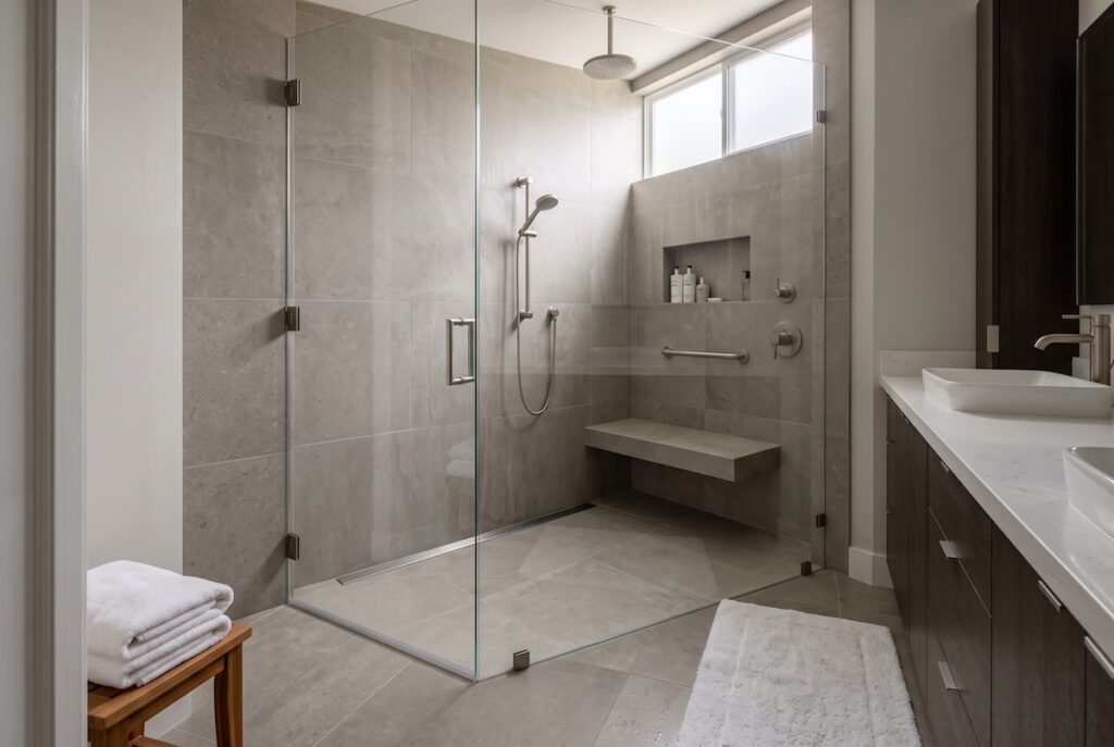 Curbless walk-in shower with a linear drain, built-in bench, dual shower heads, and a recessed niche in large-format stone tile